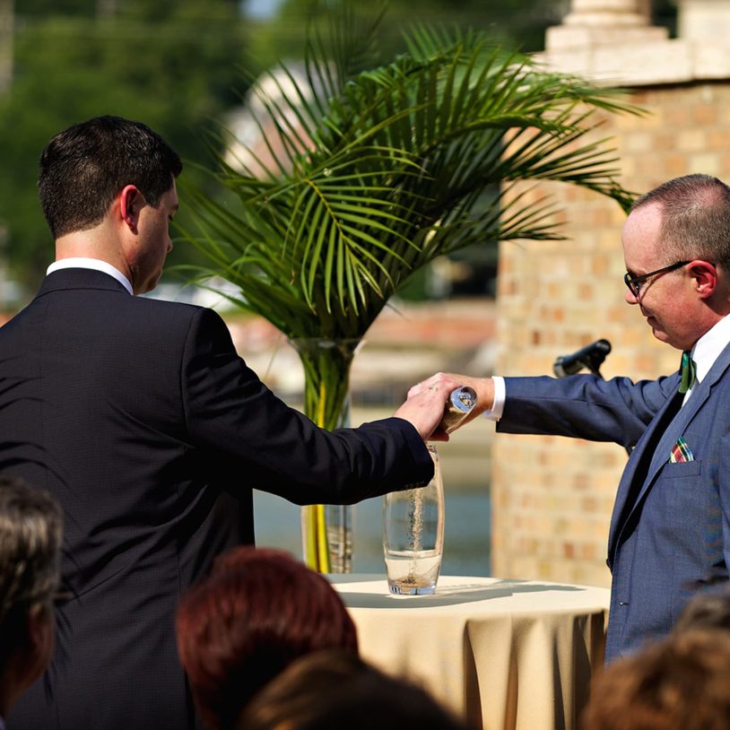 Each groom pours sand into one container at their outdoor garden wedding ceremony at wedding venue near Chicago
