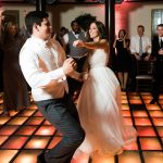 Bride and groom dance on the lighted dance floor while guest cheer them on
